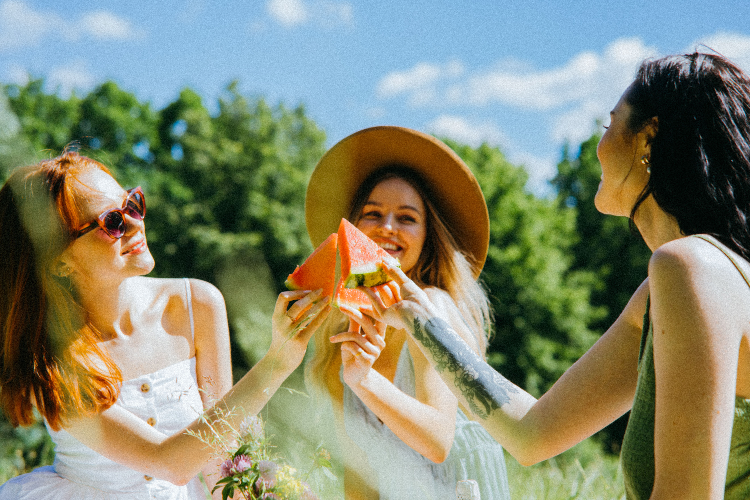 Three young women in summer clothes ready to enjoy a fresh slice of watermelon
