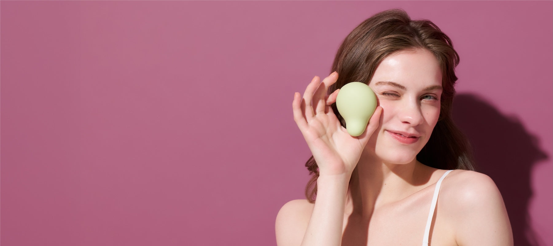 Woman holding a green iroha Midori vibrator against a pink background