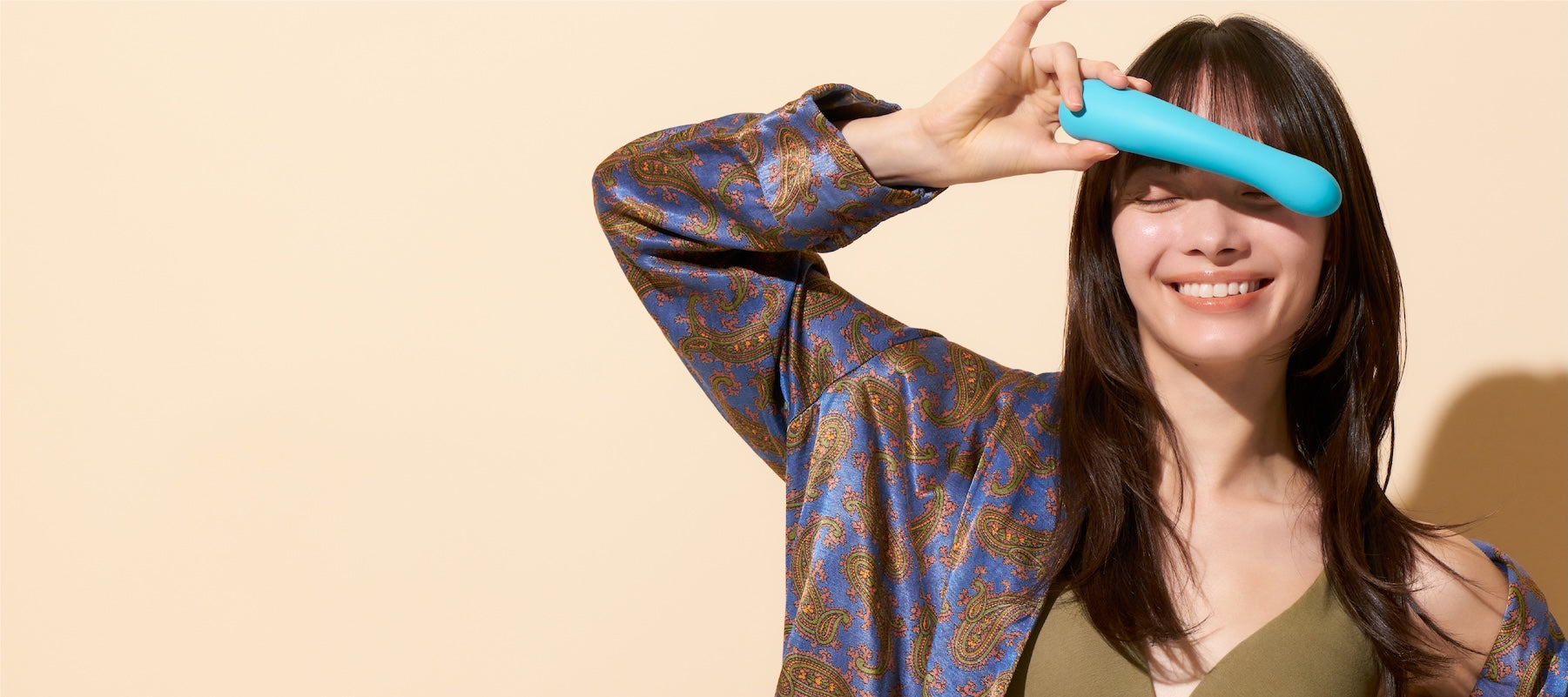 Woman holding a blue iroha TSUKI+ AONAMI vibrator against a beige background